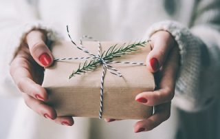 A woman's hands holding a gift wrapped in brown paper.