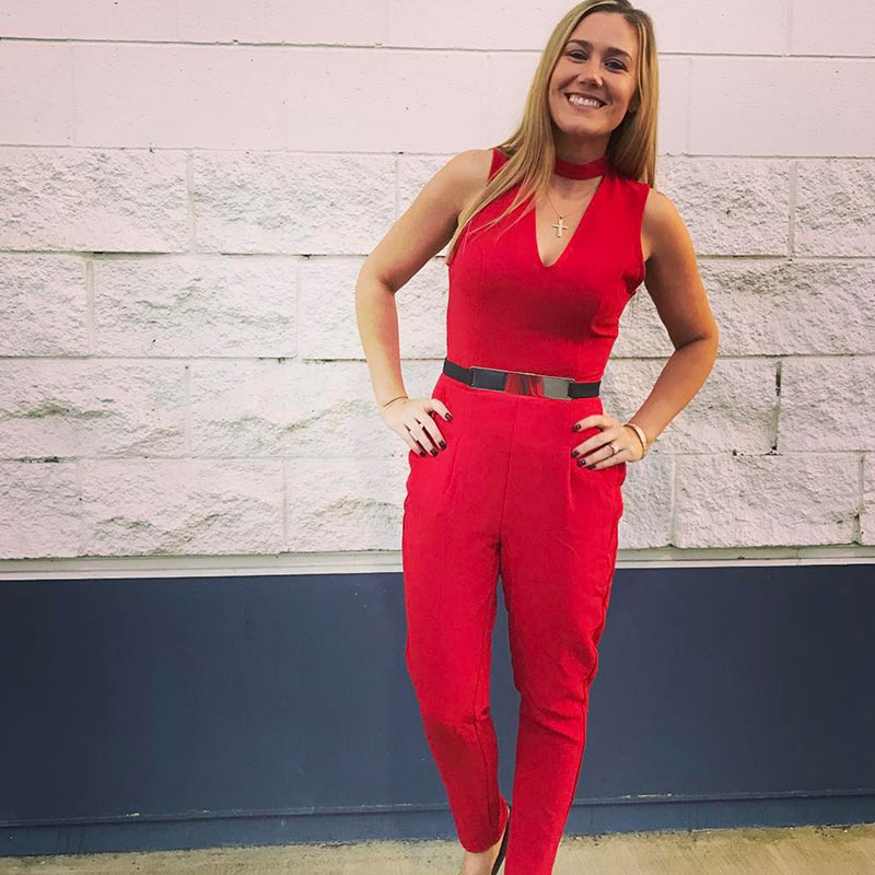 A woman in a red jumpsuit standing in front of a wall.