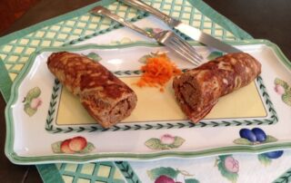 A plate with two meat rolls and carrots on it.