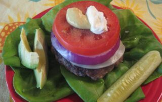 A burger topped with tomatoes, lettuce and pickles.