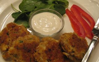 A white plate with crab cakes and a fork.