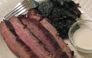 A plate of steak and greens with a fork.