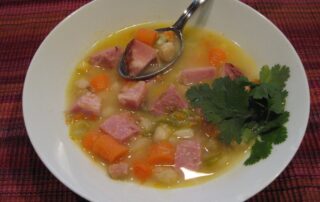 A bowl of soup with ham and carrots.