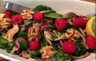 A bowl of spinach salad with walnuts and raspberries.