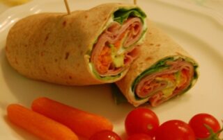 A wrap with ham, tomatoes and carrots on a plate.