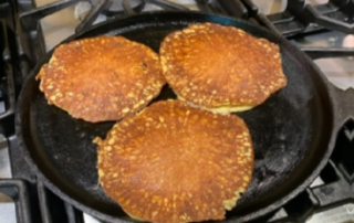 Three pancakes in a cast iron skillet on a stove.