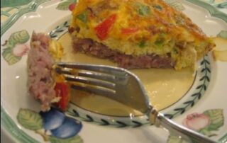 A piece of meat quiche on a plate with a fork.