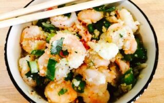 A bowl of shrimp and vegetables with chopsticks.