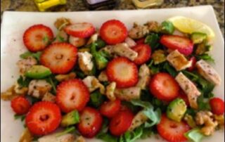 A plate of chicken salad with strawberries and walnuts.