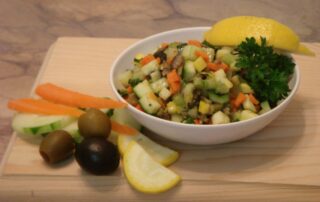 A bowl of vegetables and a lemon on a wooden cutting board.